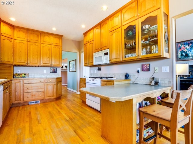 kitchen featuring kitchen peninsula, a kitchen bar, white appliances, and light hardwood / wood-style flooring