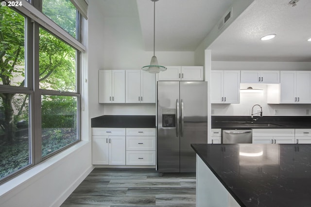 kitchen with white cabinetry, decorative light fixtures, stainless steel appliances, and a wealth of natural light