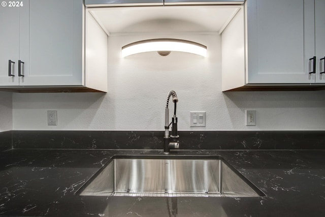kitchen featuring dark stone countertops, ornamental molding, white cabinets, and a sink