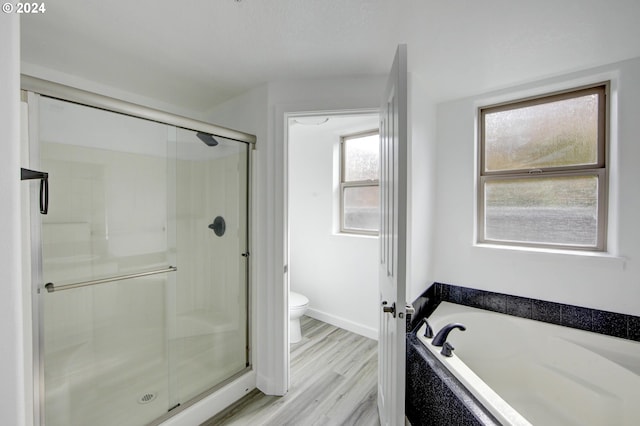 bathroom with baseboards, a stall shower, toilet, a garden tub, and wood finished floors