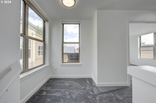 empty room featuring baseboards and dark colored carpet