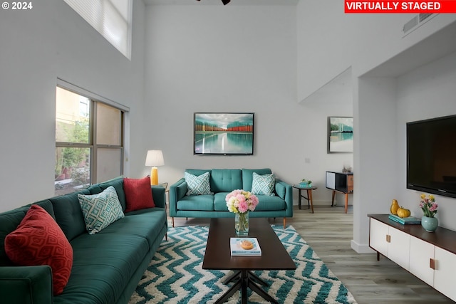 living area featuring visible vents, baseboards, light wood-type flooring, and a high ceiling