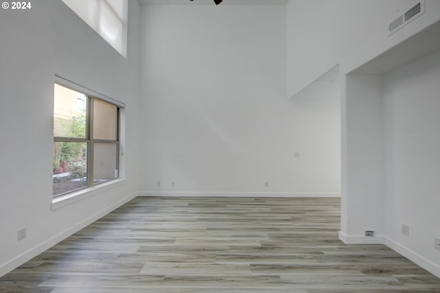 unfurnished room featuring a towering ceiling, light hardwood / wood-style floors, and ceiling fan