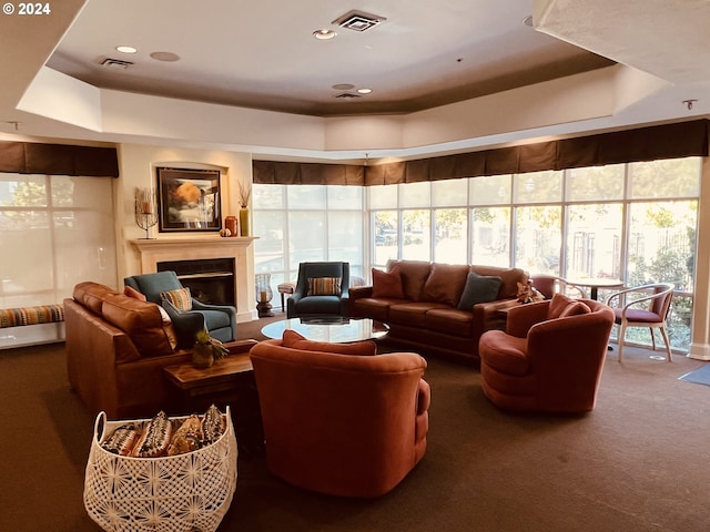 carpeted living area with a wealth of natural light, visible vents, and a raised ceiling