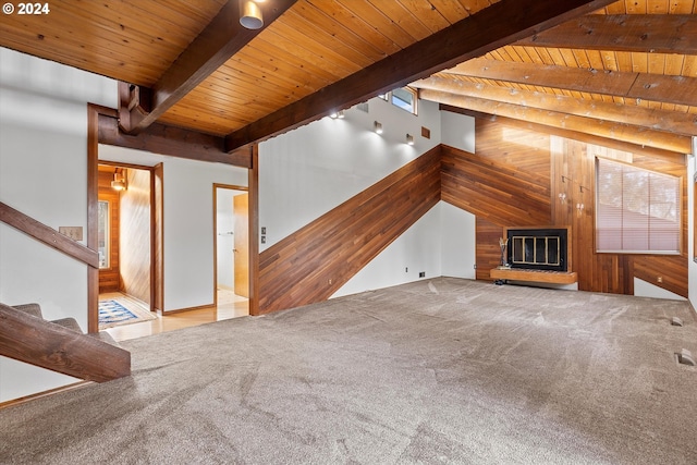 unfurnished living room with wood walls, light carpet, beamed ceiling, plenty of natural light, and wood ceiling