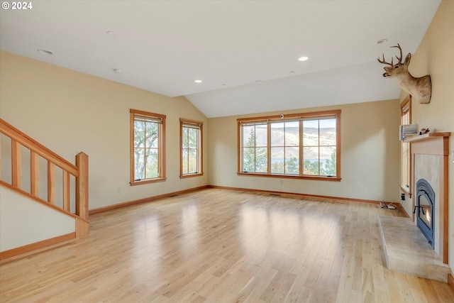 unfurnished living room with lofted ceiling, light hardwood / wood-style flooring, a tiled fireplace, and a healthy amount of sunlight