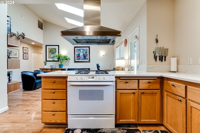 kitchen featuring white gas stove, light countertops, lofted ceiling with skylight, island range hood, and light wood-type flooring