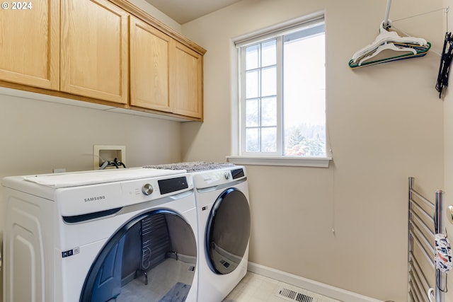 clothes washing area featuring a wealth of natural light, washer and dryer, cabinet space, and visible vents