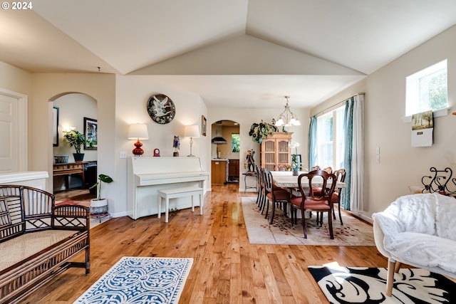 dining area with light wood-style floors, arched walkways, a chandelier, and lofted ceiling