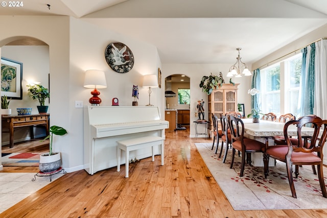 dining area with arched walkways, light wood-type flooring, baseboards, and an inviting chandelier