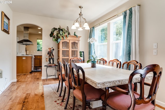 dining space featuring light wood-style floors, a chandelier, arched walkways, and a wealth of natural light