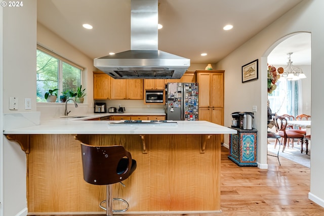 kitchen with island range hood, appliances with stainless steel finishes, a peninsula, light wood-type flooring, and a sink