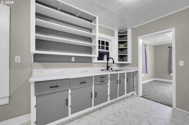 kitchen with light carpet, built in shelves, ornamental molding, gray cabinetry, and sink