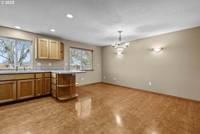 kitchen with an inviting chandelier, kitchen peninsula, a textured ceiling, sink, and decorative light fixtures