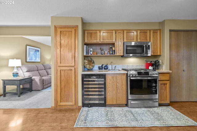 kitchen with a textured ceiling, beverage cooler, light colored carpet, appliances with stainless steel finishes, and sink