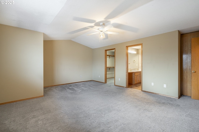 unfurnished bedroom with a closet, lofted ceiling, a walk in closet, ceiling fan, and light carpet