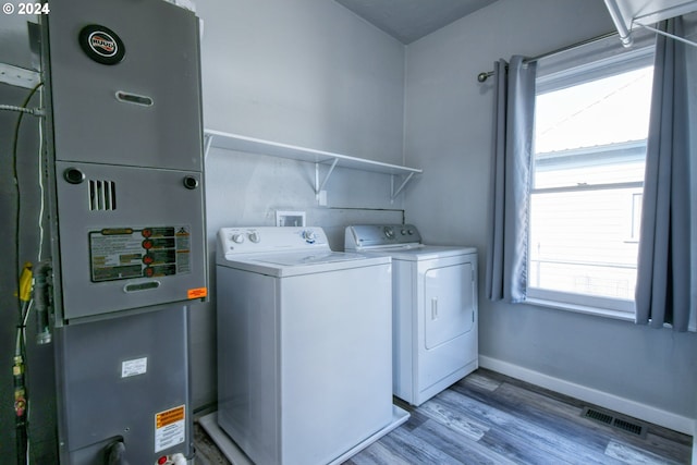 laundry room featuring heating unit, light hardwood / wood-style floors, washer and dryer, and a wealth of natural light