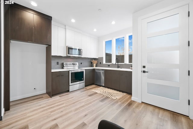 kitchen with dark brown cabinets, light wood-type flooring, appliances with stainless steel finishes, and white cabinets