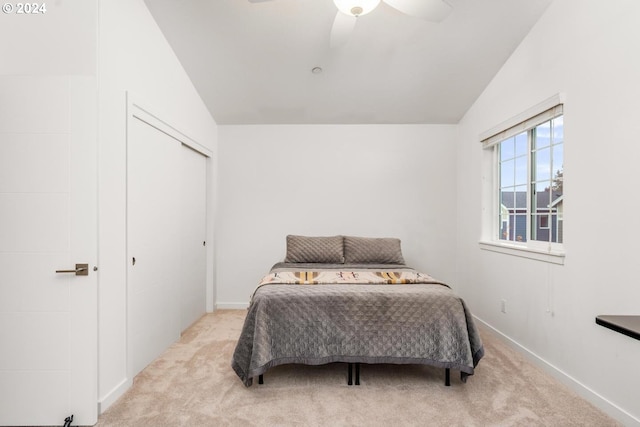 bedroom featuring ceiling fan, a closet, light carpet, and lofted ceiling