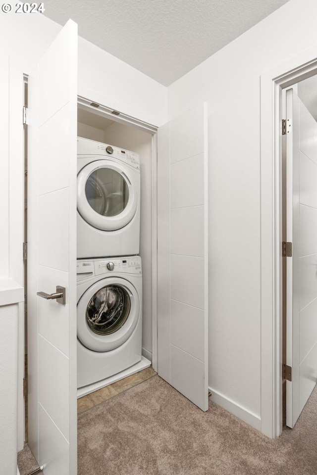 laundry area featuring a textured ceiling, light colored carpet, and stacked washer and clothes dryer