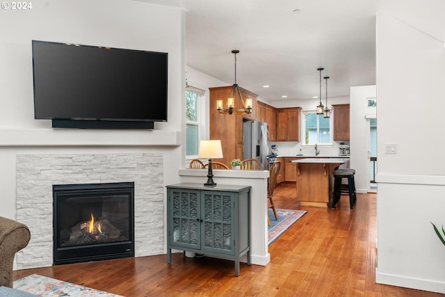 living room with a stone fireplace, light hardwood / wood-style floors, and an inviting chandelier