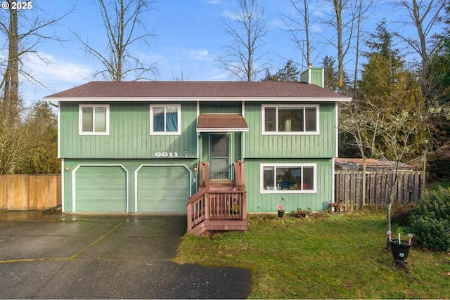 raised ranch featuring a chimney, aphalt driveway, an attached garage, fence, and a front lawn