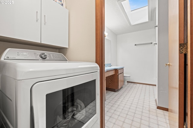 clothes washing area with a skylight, cabinet space, baseboards, washer / clothes dryer, and light floors