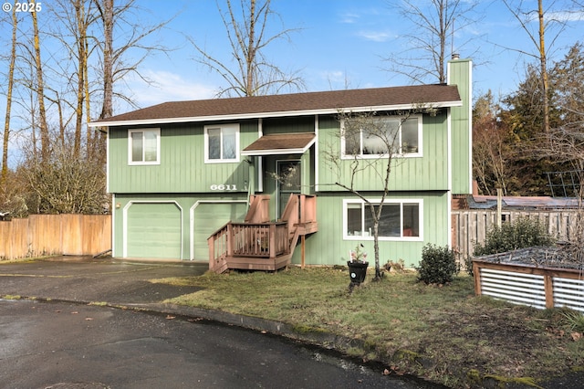 raised ranch with driveway, a chimney, roof with shingles, an attached garage, and fence