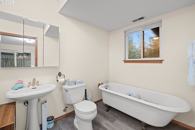 bathroom featuring a freestanding tub, toilet, visible vents, baseboards, and wood finished floors