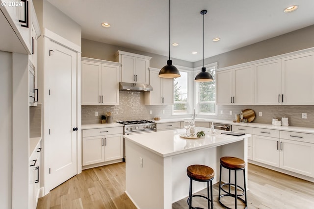 kitchen featuring white cabinets, hanging light fixtures, a kitchen island, appliances with stainless steel finishes, and light hardwood / wood-style flooring