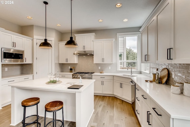 kitchen featuring appliances with stainless steel finishes, sink, light wood-type flooring, a kitchen island, and decorative light fixtures