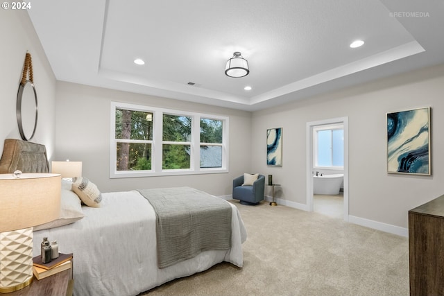 bedroom with ensuite bathroom, a tray ceiling, and multiple windows