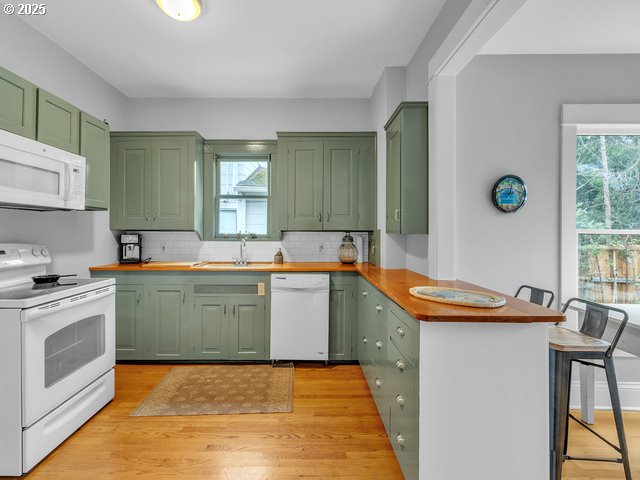 kitchen featuring a healthy amount of sunlight, white appliances, butcher block countertops, and green cabinetry