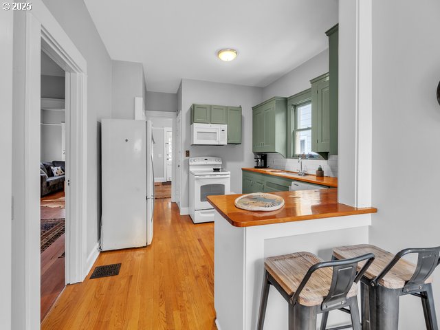 kitchen featuring a peninsula, white appliances, butcher block countertops, green cabinets, and a kitchen bar