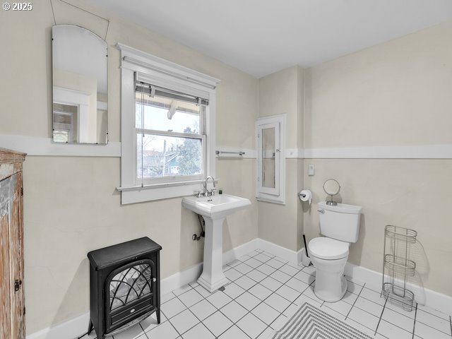 bathroom featuring toilet, a wood stove, baseboards, and tile patterned floors