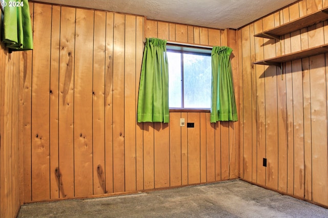 carpeted spare room featuring a textured ceiling and wood walls