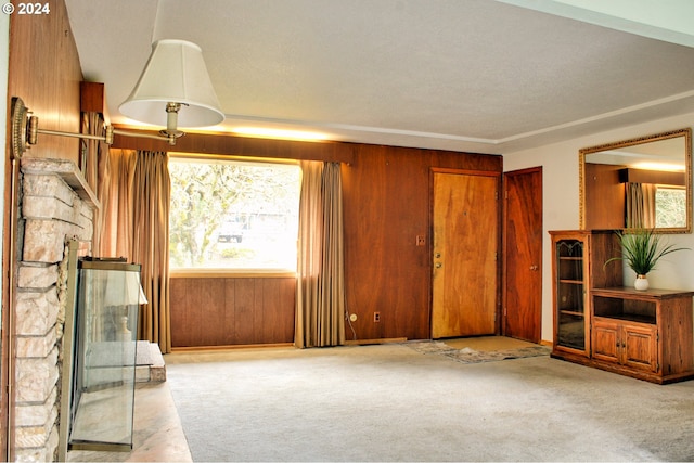 unfurnished living room featuring plenty of natural light, a stone fireplace, light colored carpet, and wooden walls