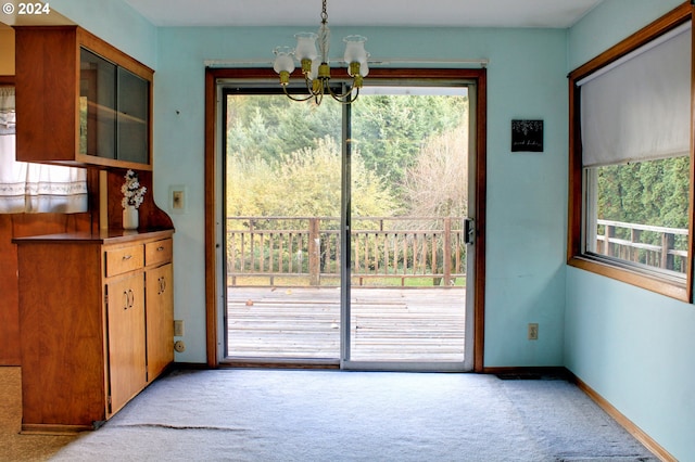 entryway with plenty of natural light, light colored carpet, and an inviting chandelier