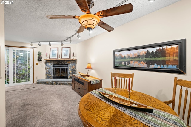 dining room with a textured ceiling, carpet floors, a stone fireplace, and ceiling fan