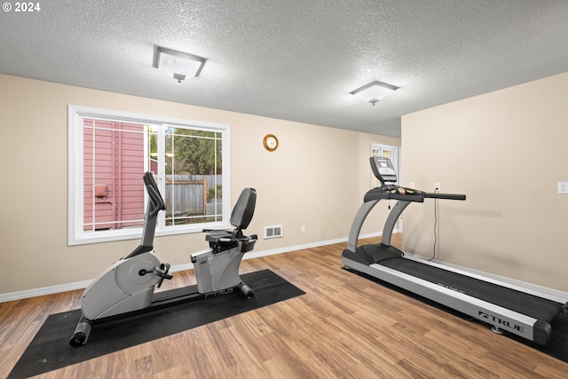 workout area featuring light wood-type flooring and a textured ceiling