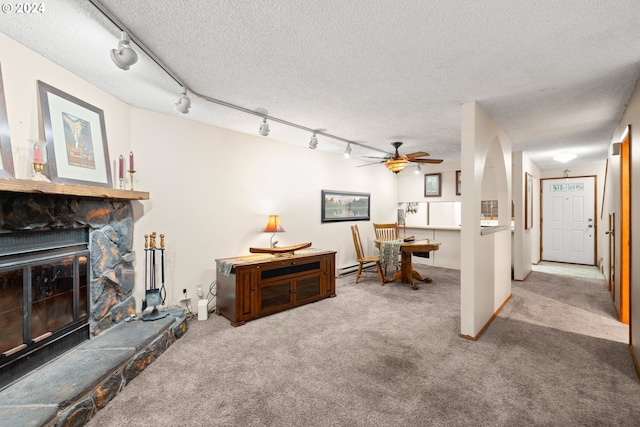 living room with carpet flooring, ceiling fan, baseboard heating, a stone fireplace, and a textured ceiling