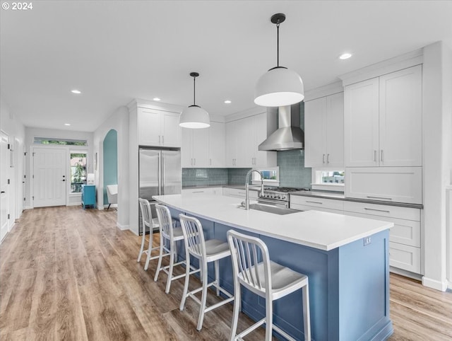 kitchen with sink, wall chimney range hood, decorative light fixtures, white cabinetry, and stainless steel refrigerator