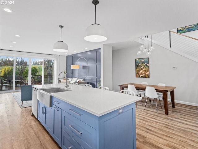 kitchen featuring sink, light hardwood / wood-style flooring, hanging light fixtures, and an island with sink