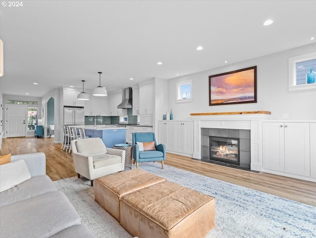 living room featuring sink, light wood-type flooring, and a tiled fireplace