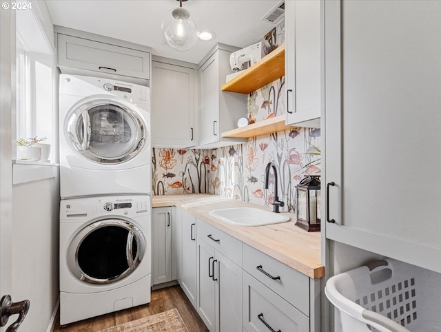 clothes washing area with dark wood-type flooring, sink, and stacked washing maching and dryer