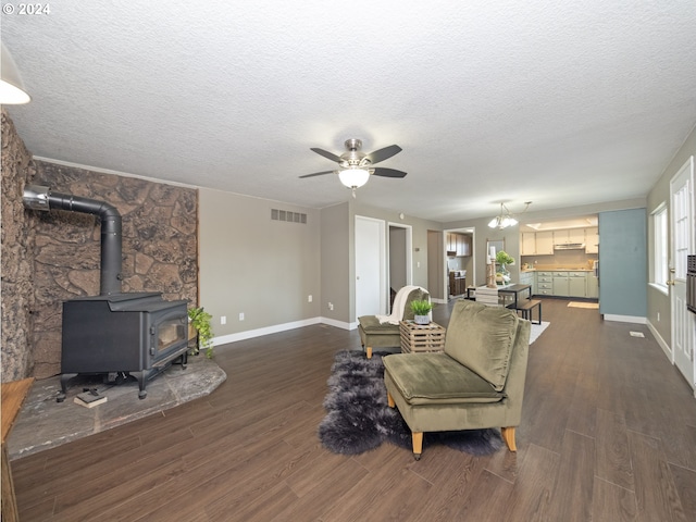 living room with ceiling fan, a textured ceiling, dark hardwood / wood-style flooring, and a wood stove