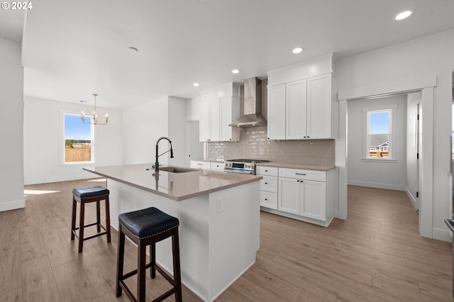 kitchen with wall chimney exhaust hood, a wealth of natural light, sink, and an island with sink