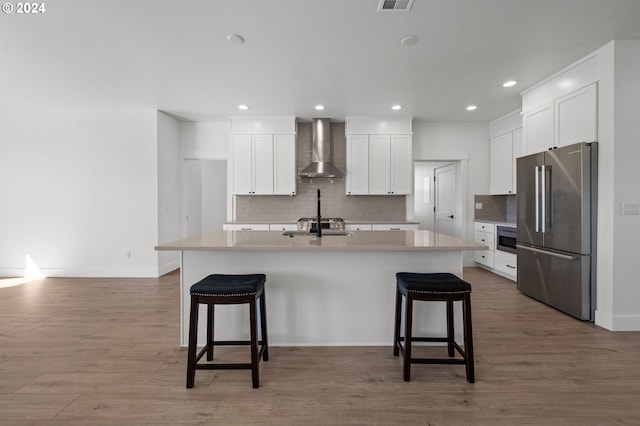 kitchen featuring white cabinetry, stainless steel appliances, wall chimney exhaust hood, hardwood / wood-style flooring, and a center island with sink