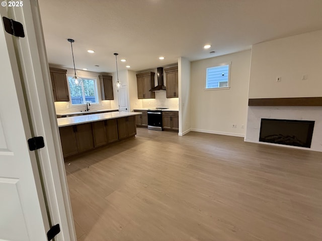 kitchen with tasteful backsplash, stainless steel range with electric cooktop, wall chimney range hood, decorative light fixtures, and light hardwood / wood-style floors