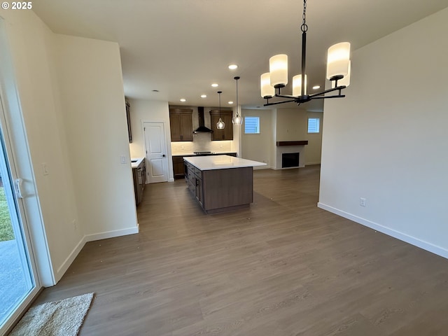 kitchen with hardwood / wood-style flooring, wall chimney exhaust hood, pendant lighting, a kitchen island, and an inviting chandelier